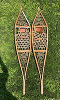 Top view of the pair of vintage Ojibwe handmade wooden snowshoes with rawhide lacing, showing full length and pointed tips.
