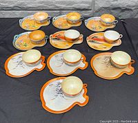Full top-down view of all nine tennis-shaped saucers with matching cups from front angle, showing unique detailed hand-painted designs and lustre finish.