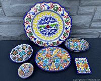 Full set of six colorful vintage Talavera pottery pieces on a black cloth background with gray stone wall