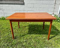 Front view of teak dining table in natural light showing rectangular top and tapered legs