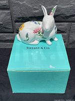Porcelain rabbit with colorful floral decorations sitting on original Tiffany & Co. blue box, showing front and side views.
