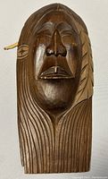 Photo of front view of the carved cedar wooden mask showing detailed facial features and feather motif.