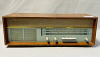 Front view of the rectangular wooden tube radio showing speaker grille, tuning scale with four control knobs and push buttons, and plastic dial cover with hairline crack.