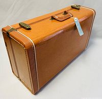 Brown suitcase resting closed with visible water stains and white corner stitching.
