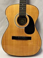 Full front view of the Anjo acoustic guitar showing the body, sound hole with label, black pickguard, and wood grain finish.