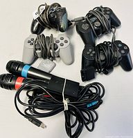Top view of three Sony PlayStation controllers with cables coiled, two SingStar microphones with cables in front.