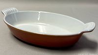 Side angle of oval dish showing white glazed interior, orange exterior, and ribbed handles.