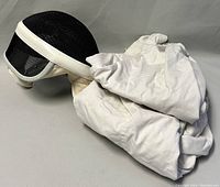 Fencing helmet placed on white fencing uniform showing helmet mesh and fabric material of uniform.