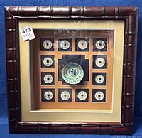 Full view of framed Chinese shadow box art showing the bamboo style frame and all coin and plate elements inside.
