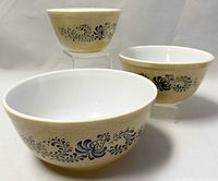 Three nesting Pyrex Homestead mixing bowls arranged with two bowls upright and one smaller one elevated.