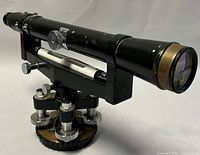 Side front view of vintage Japanese surveying transit telescope showing black tube, brass eyepiece and objective, and mechanical adjustment knobs on leveling base.