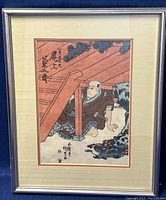Framed vintage Japanese woodblock print showing a man under a wooden structure, beige mat and blue-gray frame, minor wear