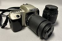 Front angled view of Nikon F50 camera with Tamron 80-210mm lens attached and 28-80mm lens nearby.