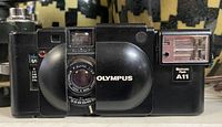 Front view showing Olympus brand name, F-Zuiko 35mm f/2.8 lens, aperture and shutter speed markings, and integrated electronic flash A11.