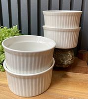 Photo of four white ribbed ceramic ramekins stacked two sets of two on a wooden surface with neutral background.