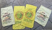 Four authentic corn feed sacks from a farm in Northern Ohio. Two sacks are off-white with red and black M & M Hybrid Seed Corn branding. Two sacks are yellow with Central States Seed Service Inc branding in red, green, and black. All sacks show vintage wear.