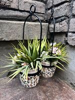 Two fake plants in mosaic pots with metal arch hangers designed for wall mounting, displayed against stone wall.