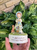 Front view of vintage Holly Hobbie music figurine showing girl in bonnet with cat and dog on base with inscription
