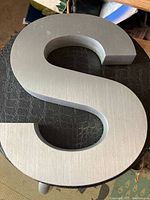 Close-up photo of a thick metal letter S showing the brushed steel texture and substantial size.