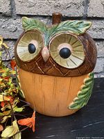 Front view of ceramic owl figurine showing large eyes, leaf accents, and painted details.