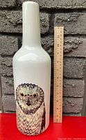 Front view of the white ceramic vase with detailed owl illustration next to a ruler showing approx. 12 inches tall.