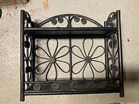 Front view of black painted rattan wall shelf with floral design and two shelves.