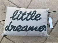 Front side of pillow showing cream fabric with black embroidered text "little dreamer" in cursive.
