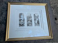 Full view of the framed art piece showcasing three vertical panel prints of architectural scenes inside a gold frame.
