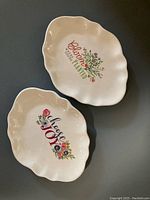 Photo showing two white ceramic trinket dishes with scalloped edges and floral inscriptions.