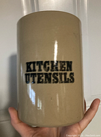 Photo of beige ceramic kitchen utensil crock with 'KITCHEN UTENSILS' written in black on the front.
