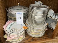 Stacked plates, bowls, and cups with visible floral and gold trim pattern inside a wooden cabinet.