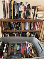 Photo showing variety of books arranged on shelve with some in storage bin, covers visible including titles on history, fantasy and sports