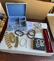 Full view of jewelry box with multiple bracelets and some chains or necklaces, all laid on a white box