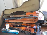 Violin and guitar in cases placed on table with recorder and bows.