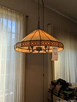 Craftsman style hanging lamp illuminated, showing amber and cream faux stained glass shade with geometric pattern band.