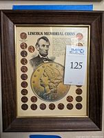 Framed display containing 29 Lincoln Memorial pennies arranged in a circle around a portrait of Abraham Lincoln and an illustrated old coin. Text on the display provides historical context about the Lincoln Memorial coin series.