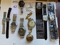 Full view of all watches and stopwatch laid out on table including Eiger watches, Rosine stopwatch, gold tone pocket watch with quarter, Stauer chronograph, Casio watch, Embassy watch, and Seiko band.