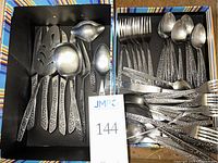 Two black boxes containing the flatware pieces with embossed floral pattern handles displayed clearly showing spoons, forks, knives, and serving utensils.
