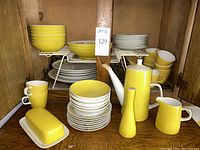 Mixed Mikasa Elite dishes and solid yellow serve pieces arranged on wooden shelf