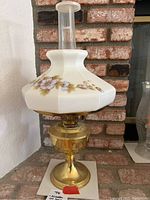 Full view of the vintage Aladdin oil lamp showing the brass base, floral glass shade, and clear glass chimney with Aladdin branding.