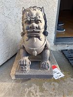 Front view of male lion statue on square base, ball under paw