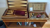 Two wooden backgammon game boards opened, showing playing field and pieces inside, including two dice cups and a velvet pouch.