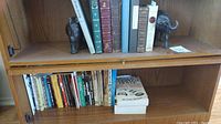 Wide view of bookshelf showing various hardcover and paperback books and two figurines (elephant and rhinoceros). Books cover diverse topics including poetry, novels, and casino game strategy.