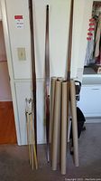 Three wooden bows leaning against wall with six cardboard tubes and tripod stand to the right