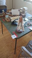 Card table and various items on top including model space shuttle and wooden boxes.