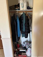Closet containing coats, jackets, scarves hanging on hangers, and shoes on the floor beneath.