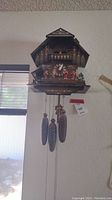 Front view of chalet style cuckoo clock showing shingled roof, balcony, figurines and pinecone weights