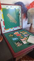 Open boxed Franklin Mint Monopoly game with green felt-lined board and organized compartments for cards, money, and metal pieces.