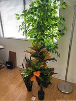 Wide view of all three faux plants in room near window and floor lamp.