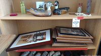 Multiple wooden picture frames stacked and arranged on a shelf with wooden duck decoys and various decorative items.